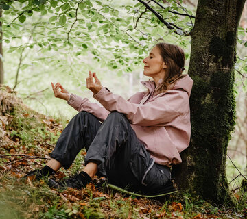 Eine Frau lehnt an einem Baum und meditiert