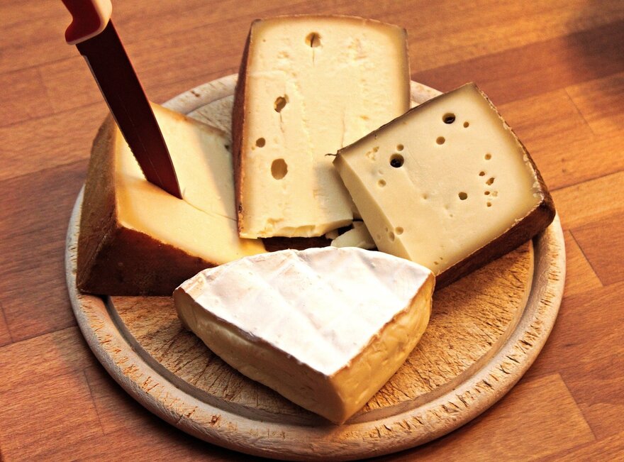 Die Abbildung zeigt eine hölzerne Schneidebrett mit verschiedenen Arten von Käse auf ihm. Der Käse ist geschnitten und auf dem Brett arrangiert.