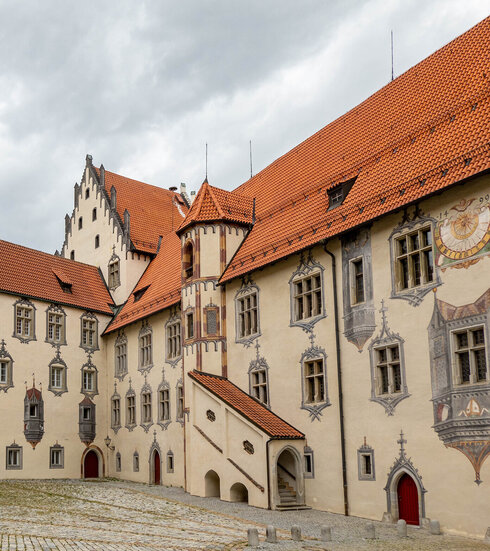 Innenhof eines mittelalterlichen Schlosses mit roten Dächern und markanten Fachwerkkonstruktionen.