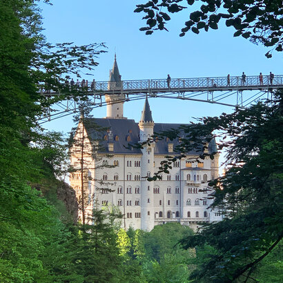 Das Foto zeigt im Vordergrund die Marienbrücke mit einigen Besuchern, dahinter Schloss Neuschwanstein bei Füssen im Allgäu.