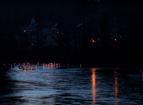 Neujahrsschwimmen Das Bild zeigt einen dunklen Fluss. Über ihm sind die Umrisse von Häusern in der Dunkelheit zu erkennen. Auf dem Fluss schwimmt eine sehr große beleuchtete „2018“ im Hintergrund schwimmen zahlreiche Menschen mit brennenden Fackeln.