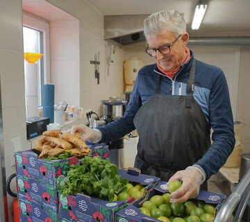 Ein Mann steht vor einigen Kartons, die mit den Zutaten für den AlpenZenzero-Sirup, Ingwer, Minze und Limetten, gefüllt sind.