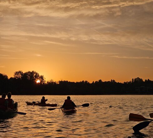 eine Gruppe Kanufahrer treibt entspannt auf dem Forggensee beim Sonnenuntergang.
