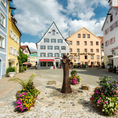 Der Schrannenplatz in Füssen mit historischen Gebäuden und Blumenkästen. Ein idyllischer Ort im Herzen der Stadt.