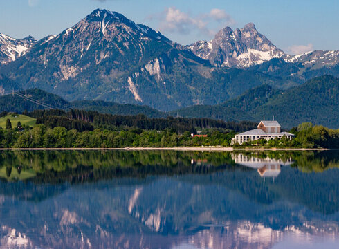 Das Foto zeigt das Festspielhaus Neuschwanstein am Forggensee mit den umliegenden SAlpengipfeln im Hintergrund.