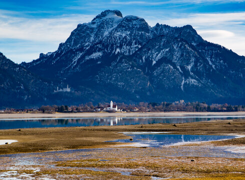 Blick über den teilweise abgelassenen Forggensee auf Schloss Neuschwanstein und den Säuling.