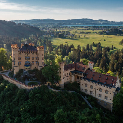 Das prächtige Schloss Hohenschwangau thront auf einem Hügel inmitten einer grünen Landschaft. Die Aussicht bietet eine idyllische Kulisse.