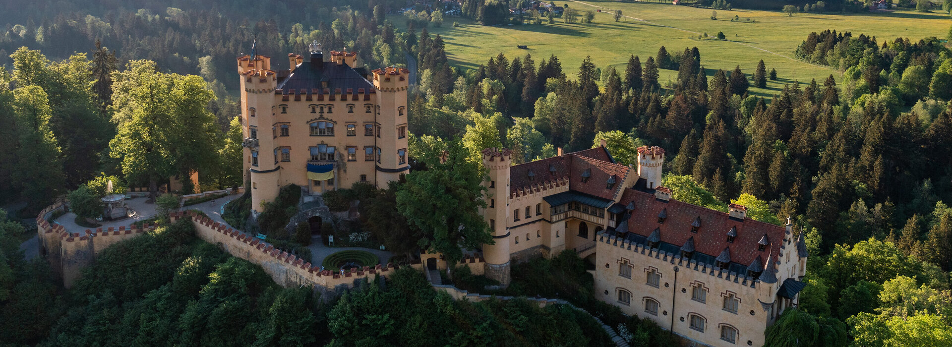 Das prächtige Schloss Hohenschwangau thront auf einem Hügel inmitten einer grünen Landschaft. Die Aussicht bietet eine idyllische Kulisse.