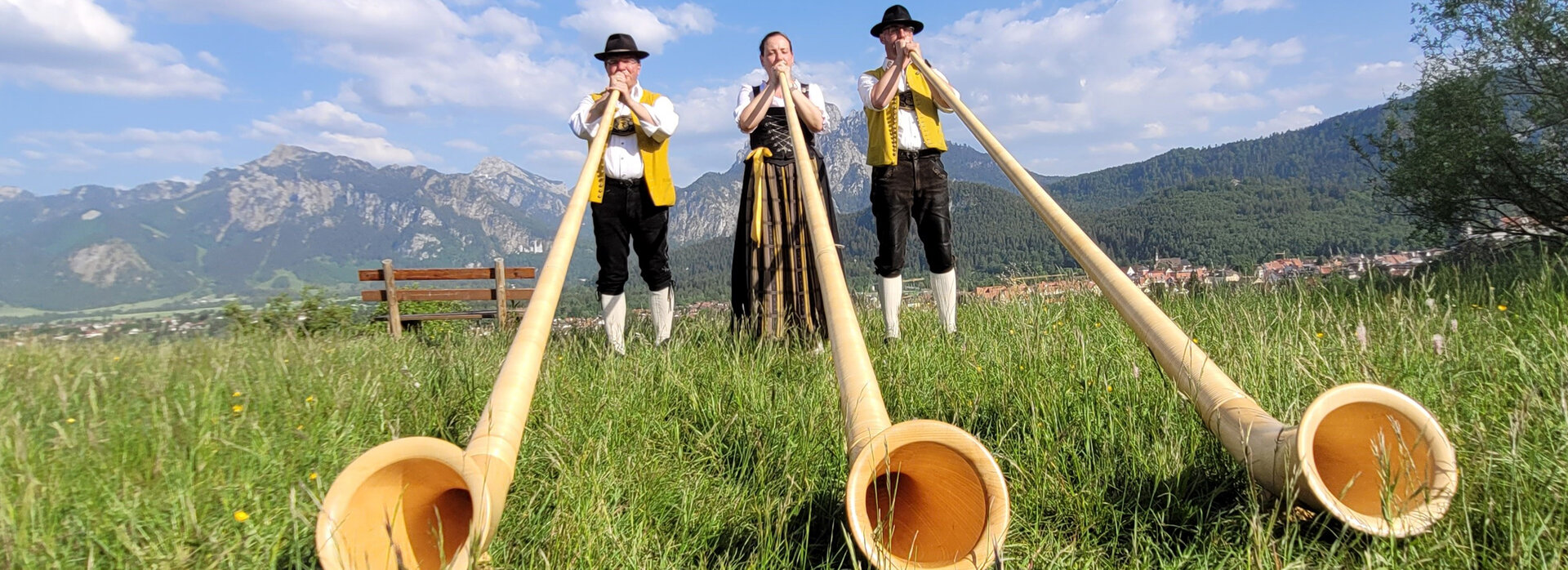 Drei Alphornbläser spielen auf einer Wiese ihre Alphörner