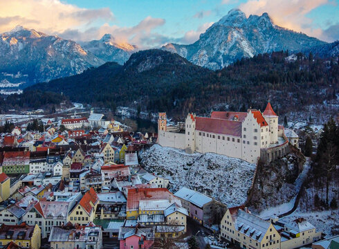 Die Luftaufnahme zeiget die winterliche Altstadt von Füssen mit verschneiten Alpengipfeln im Hintergrund.