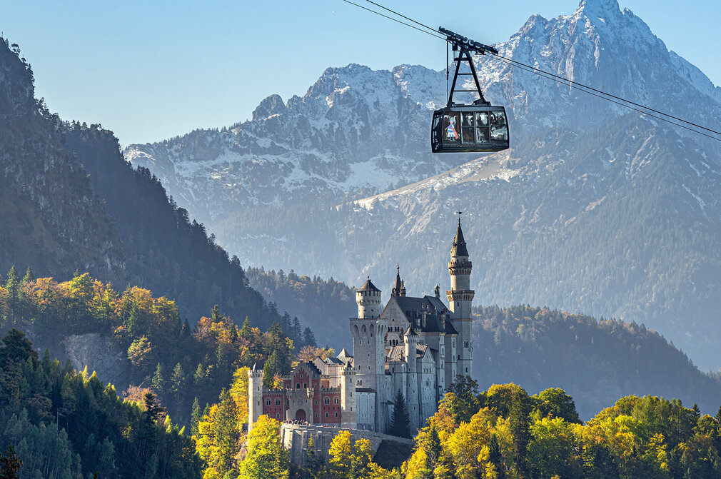 Eine Kabine der Tegelbergbahn gleitet am Schloss Neuschwanstein vorbei. Im Hintergrund ist der majestätische Säuling (2047m).