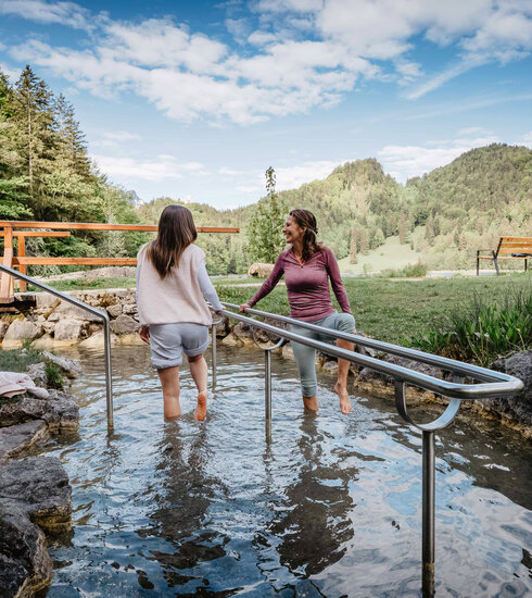 Das Bild zeigt zwei Frauen, die in einem Naturkneippbecken Wasser treten