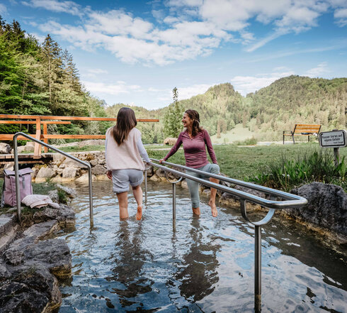 Das Bild zeigt zwei Frauen, die in einem Naturkneippbecken Wasser treten