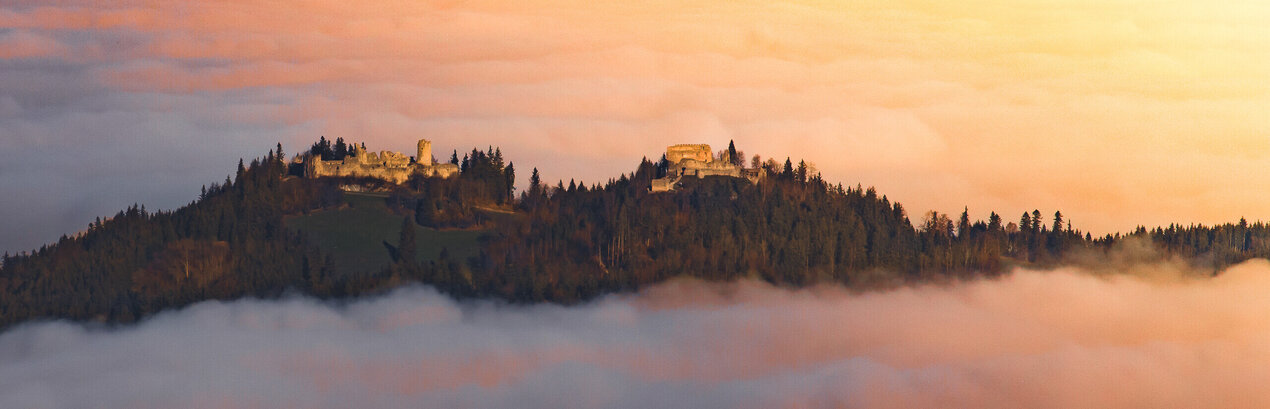 Eine Burgruine schmiegt sich in den Nebel, ein Ort voller Geschichten und Geheimnisse. Ein atemberaubender Sonnenuntergang verstärkt die mystische Stimmung.