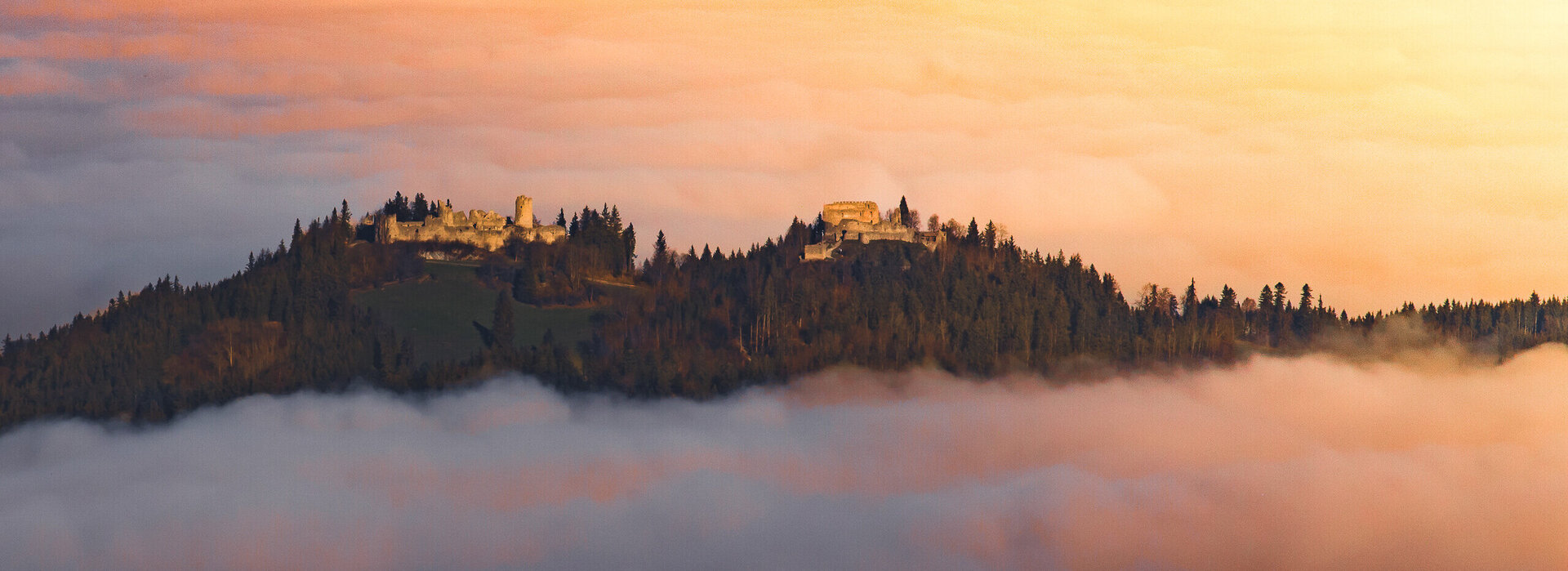 Eine Burgruine schmiegt sich in den Nebel, ein Ort voller Geschichten und Geheimnisse. Ein atemberaubender Sonnenuntergang verstärkt die mystische Stimmung.