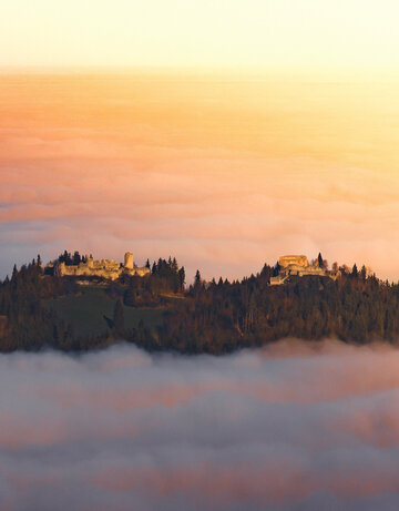 Eine Burgruine schmiegt sich in den Nebel, ein Ort voller Geschichten und Geheimnisse. Ein atemberaubender Sonnenuntergang verstärkt die mystische Stimmung.