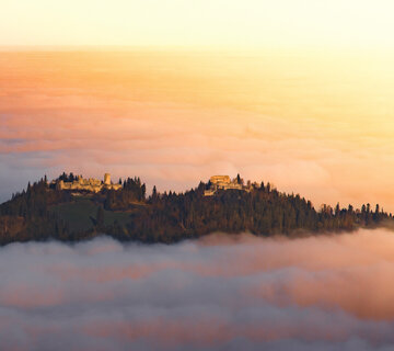Eine Burgruine schmiegt sich in den Nebel, ein Ort voller Geschichten und Geheimnisse. Ein atemberaubender Sonnenuntergang verstärkt die mystische Stimmung.