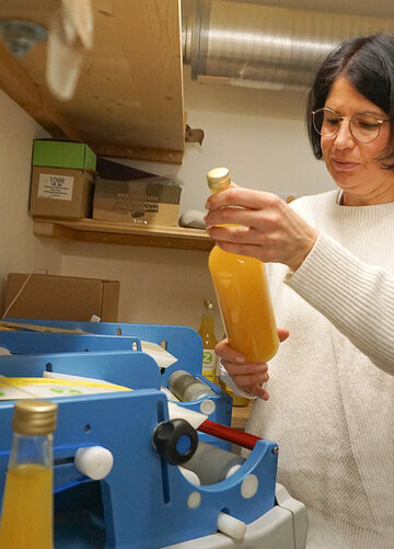 Eine Frau steht vor der Etikettiermaschine und hält eine Flasche mit gelbem AlpenZenzero-Sirup in der Hand.