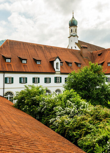 Historisches Klostergebäude mit markanten Dächern und grüner Umgebung.