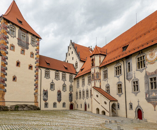 Innenhof eines mittelalterlichen Schlosses mit roten Dächern und markanten Fachwerkkonstruktionen.