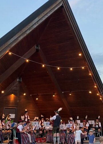 Im Pavillon welches mit Lichterketten dekoriert ist speilen die Musiker ihren geliebten Dämmershoppen. Im Vordergrund sind zwei Kinder zu sehen, welche Spaß an der Musik haben.
