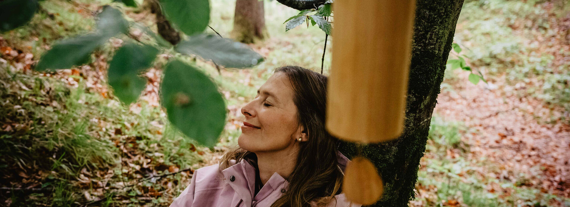 Eine Frau lehnt an einem Baum und lauscht einem Windspiel