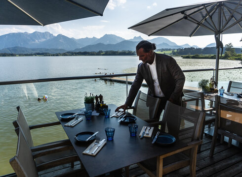 Das Foto zeigt die Terrasse vom Seehaus Hopfensee mit Blick auf den See und die Berge.