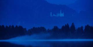 Blick über den Forggensee auf das königliche Schloss Neuschwanstein bei Abenddämmerung.