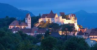Blick auf das beleuchtete Hohe Schloss bei Abenddämmerung in der romantischen Füssener Altstadt.